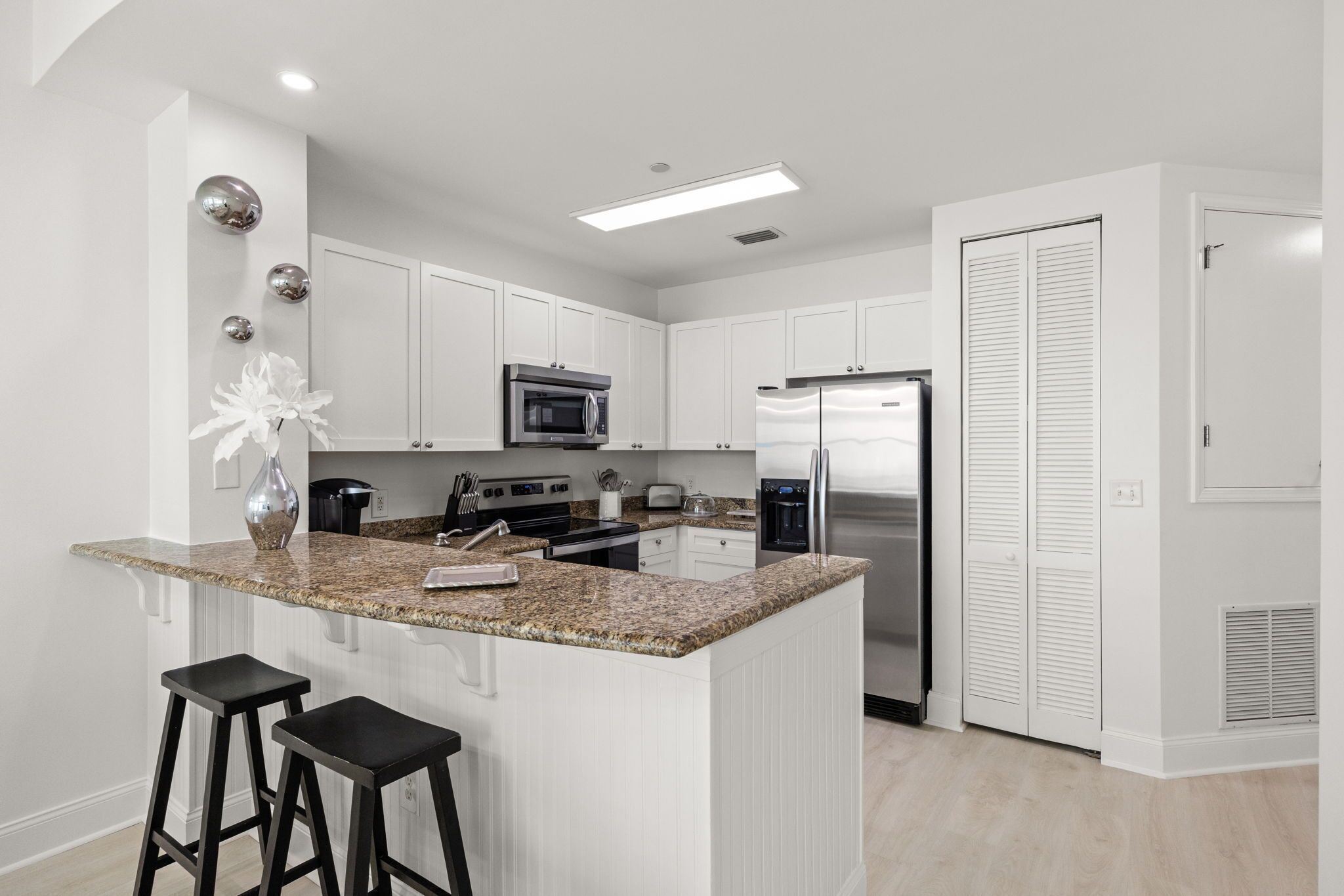 A modern kitchen with white cabinetry, a granite countertop, stainless steel appliances, and a bar stool.