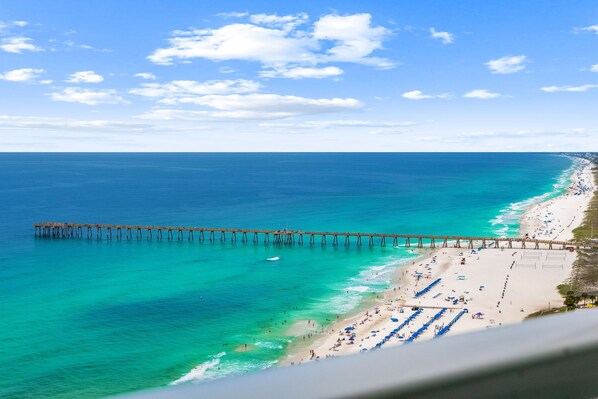 A beach with a pier extending into the ocean, clear skies, and a sandy shoreline with umbrellas. - Aqua 2310 PCB at its Finest/Oceanfront/ High Clean Standard/Wifi (Panama City Beach)