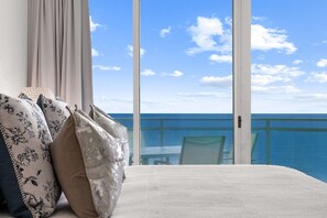 A hotel room with a large window, a bed with floral pillows, and a view of the ocean. - Aqua 2310 PCB at its Finest/Oceanfront/ High Clean Standard/Wifi (Panama City Beach)