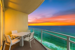 A balcony with a table and chairs, overlooking a body of water with a sunset. - Aqua 2310 PCB at its Finest/Oceanfront/ High Clean Standard/Wifi (Panama City Beach)