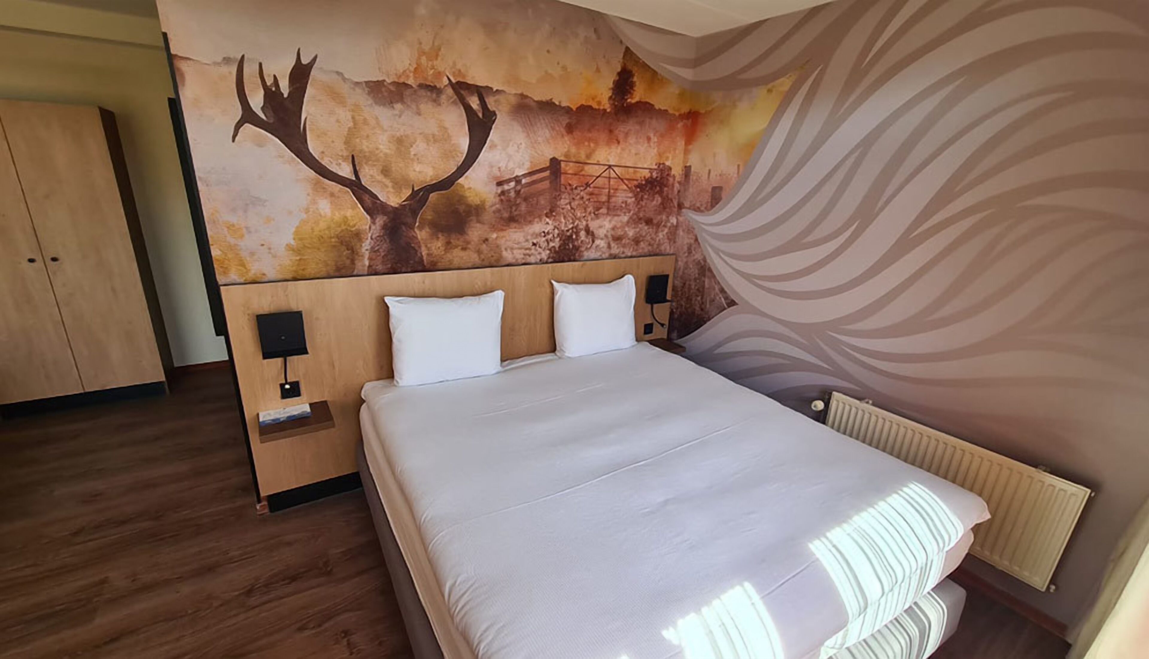 Ein Schlafzimmer mit Bett, Holz-Kopfteil, Nachttischen und einer Wandmalerei.