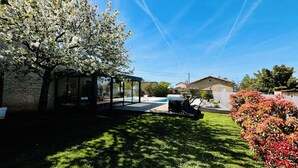 A backyard with a covered seating area, a swimming pool, and a house in the background.