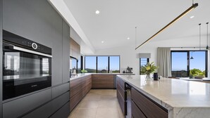A modern kitchen with a Bosch oven, dark cabinetry, a marble countertop, and large windows offering a view of the landscape. - Scenic House With Private Yard & BBQ Area (Springbrook)