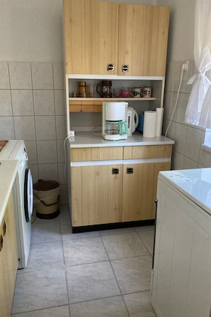 Eine kleine Küche mit Holzausstattung, einer Kaffeemaschine, einem Wasserkocher und einer Waschmaschine.