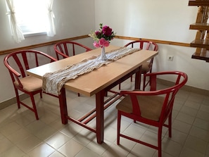 Ein Essbereich mit einem Holztisch, vier roten Stühlen, einer weißen Tischläufer mit Spitzenmuster und einer Vase mit Blumen.