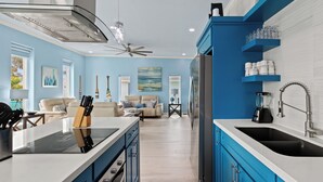 Een moderne keuken met blauwe kastjes, een centraal eiland en een zithoek met een beige bank.