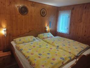 Une pièce aux murs lambrés, dotée d’un lit double, de deux lampes fixées au mur et d’une fenêtre ornée de rideaux légers.