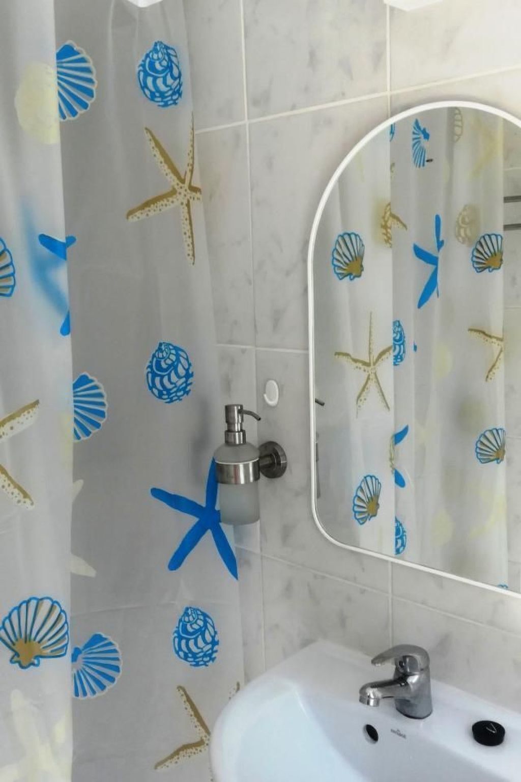 Een badkamer met een witte wastafel, een spiegel en een douchegordijn met afbeeldingen van zeeschelpen en zeesterren.
