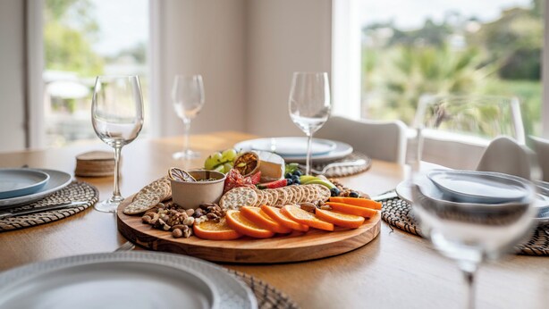 Ein Tisch, gedeckt für eine Mahlzeit, mit einer Wurstplatte, Weingläsern und Tellern.