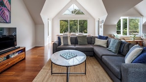 Ein geräumiges Wohnzimmer mit einer großen Eckcouch, einem runden Couchtisch und einem Fernseher auf einem Holzgestell.