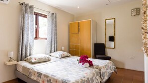 Ein Doppelbett mit floralem Bettzeug, ein Nachttisch mit Lampe, ein Kleiderschrank, ein Spiegel und ein dekoratives Wandbild.