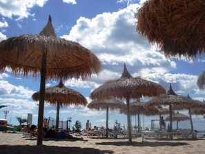 Uma praia com guarda-sóis de palha e espreguiçadeiras.