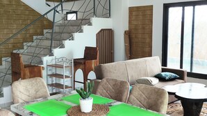 A modern living room with a staircase, a dining area with a table and chairs, and a sofa. - Villa Macarena (Bonoua)