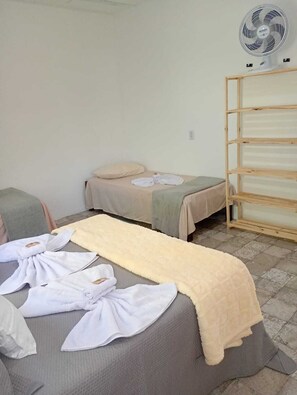 A room with two beds, a wooden shelf unit, and a standing fan. - Iza's Cozy House: Two-bedroom house, 7-minute walk from Tucuns Beach. (armaçao dos buzios)