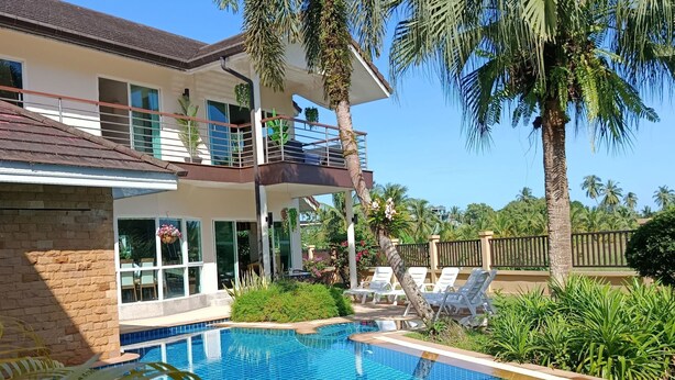 Una casa moderna de dos pisos con piscina, rodeada de palmeras y abundante vegetación.