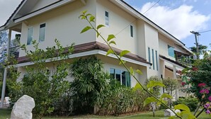 Una casa de dos plantas con techo inclinado, ventanas amplias y un jardín cuidado con diversas plantas y césped.
