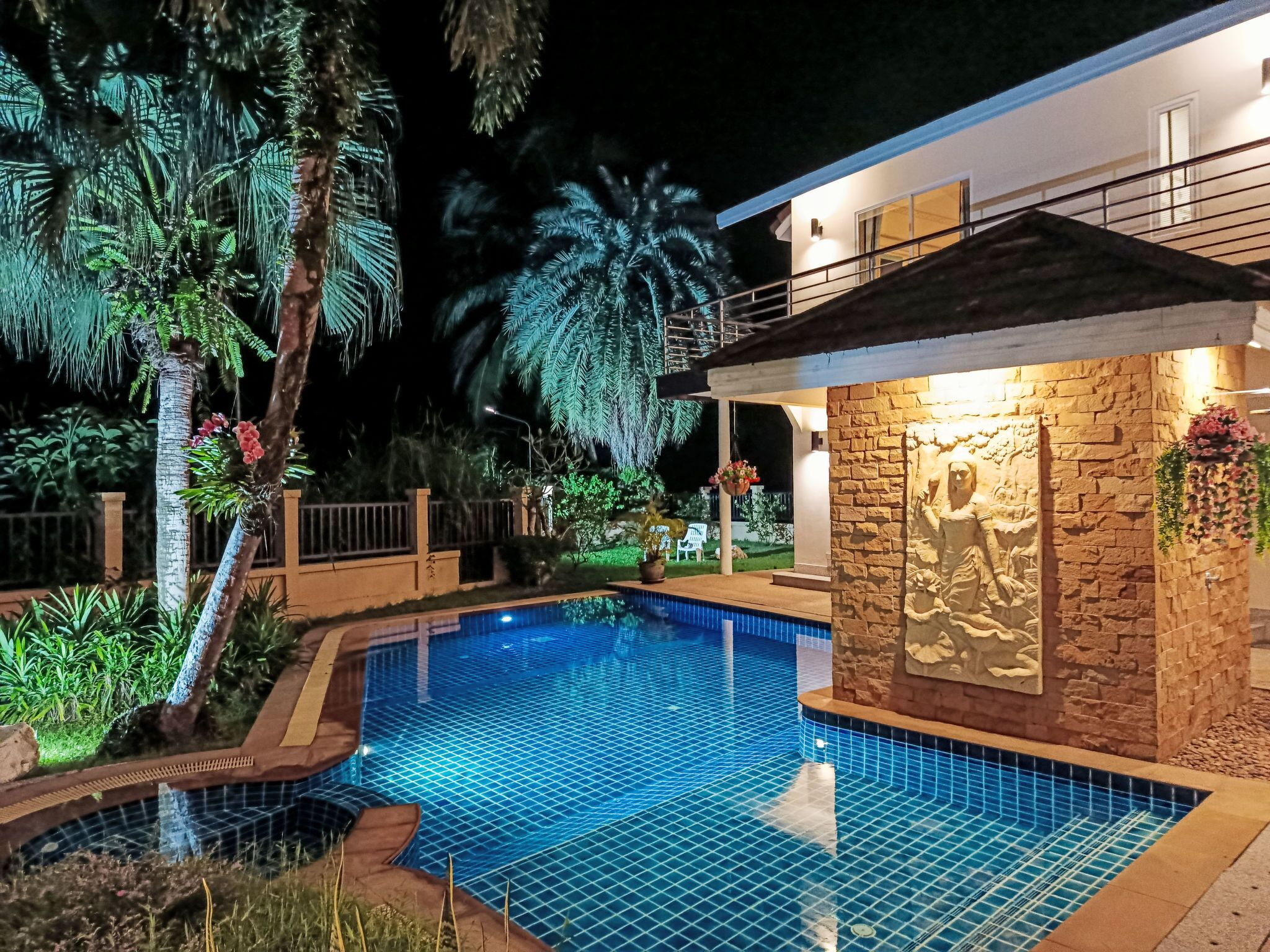 A swimming pool with a tiled edge, surrounded by tropical plants and a stone wall.