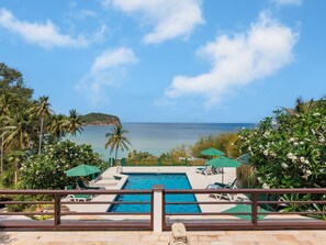 Ein Pool mit Blick auf den Ozean, umgeben von Palmen und Liegestühlen.