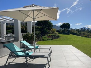 A patio area with lounge chairs and a large umbrella, overlooking a well-maintained lawn and distant mountains. - in Bos En Dal mit Großer Terrasse by Interhome (George)