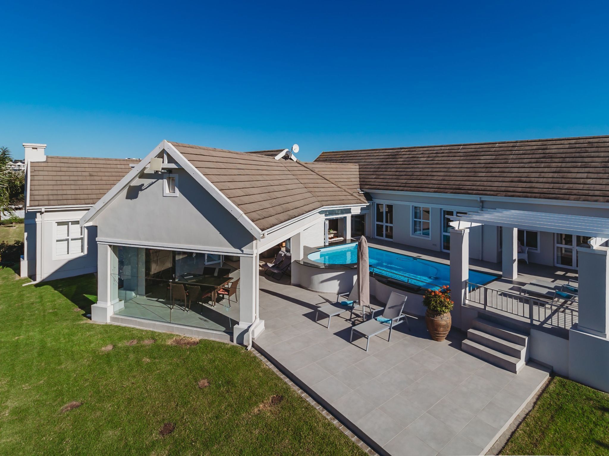 Ein modernes Haus mit überdachter Terrasse, Schwimmbad und gepflegtem Rasen.