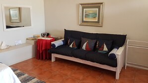 A room with a dark-colored sofa, a red table, a mirror, and a framed picture on the wall. - Sunbirdview Gästehaus by Interhome (Langebaan)