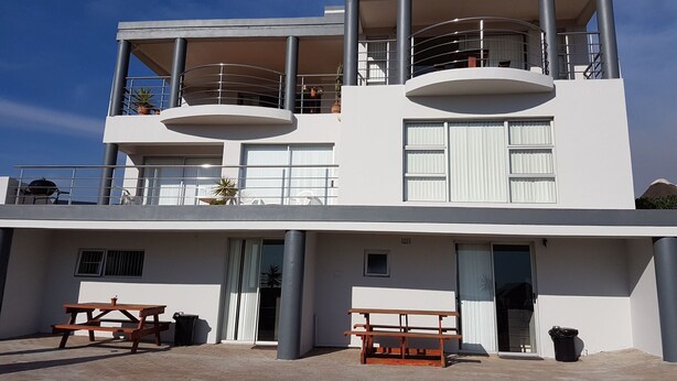 A modern multi-story building with balconies, a covered patio area, and outdoor seating. - Sunbirdview Gästehaus by Interhome (Langebaan)