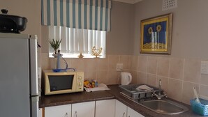 A kitchen with a refrigerator, microwave, sink, and a window with a striped curtain. - Sunbirdview Gästehaus by Interhome (Langebaan)