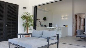 Ein modernes Wohnzimmer mit einem grauen Sofa, einer Topfpflanze und einer Glastür, die in einen Küchenbereich führt.