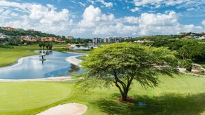 Ein Golfplatz mit Teich, Baum und Gebäuden im Hintergrund.