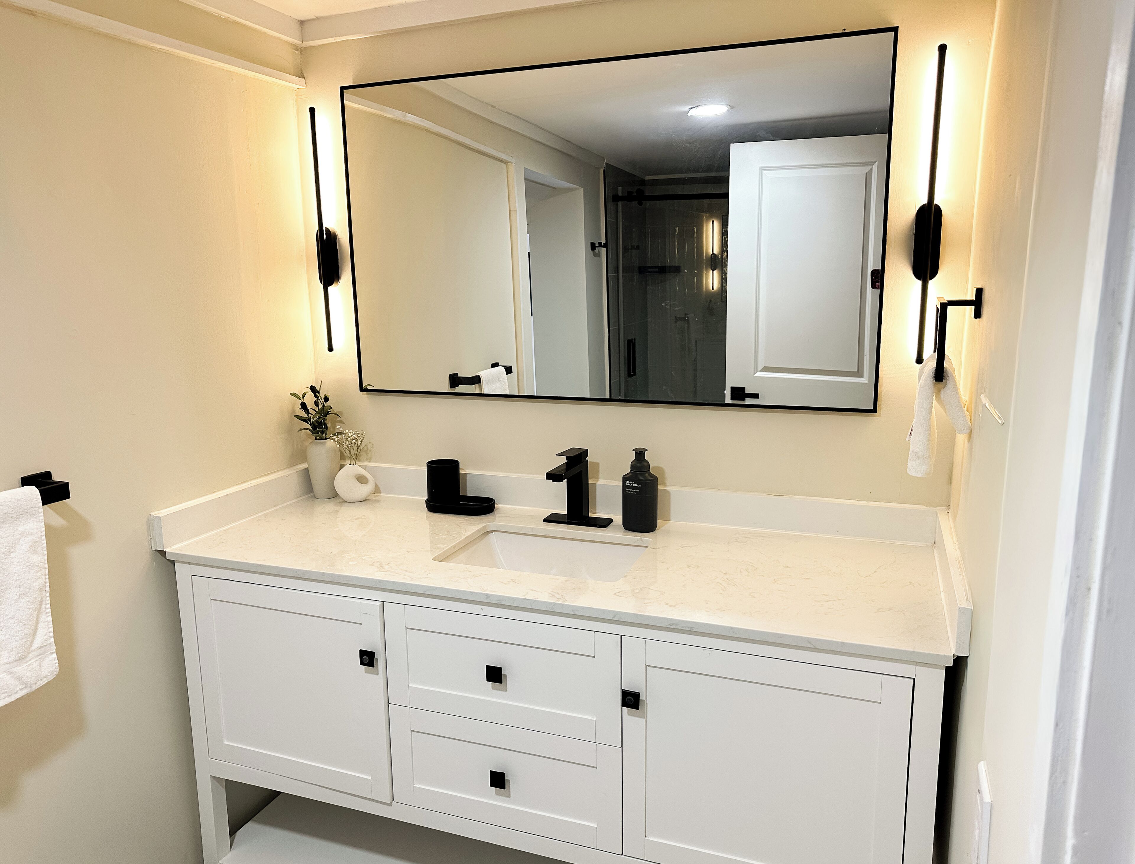 A bathroom with a white vanity, a large mirror, and a towel hanging on the wall.
