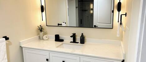 A bathroom with a white vanity, a large mirror, and a towel hanging on the wall.