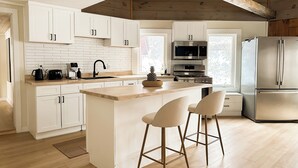 Une cuisine moderne avec des meubles blancs, un îlot central doté de tabourets de bar, un réfrigérateur en acier inoxydable et un plafond en bois.