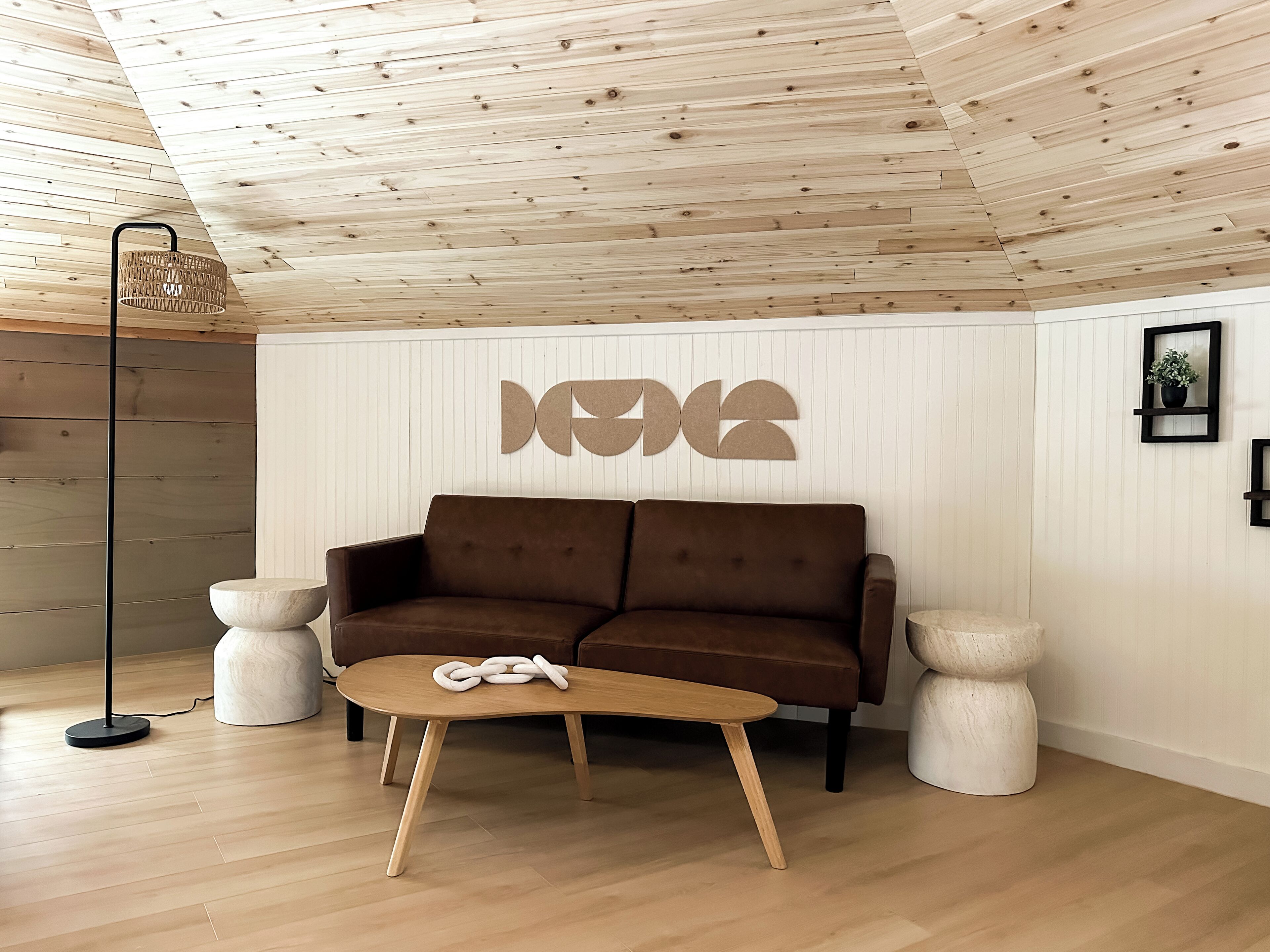 Un salon moderne avec un plafond en bois, un canapé marron, une table basse en bois et un lampadaire.