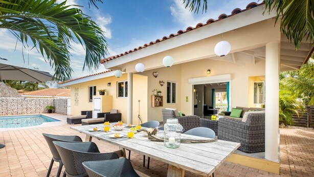 A covered outdoor dining area with a pool, wicker furniture, and a white table. - Villa Drumi Dushi met privé zwembad by Interhome (Jan Thiel)