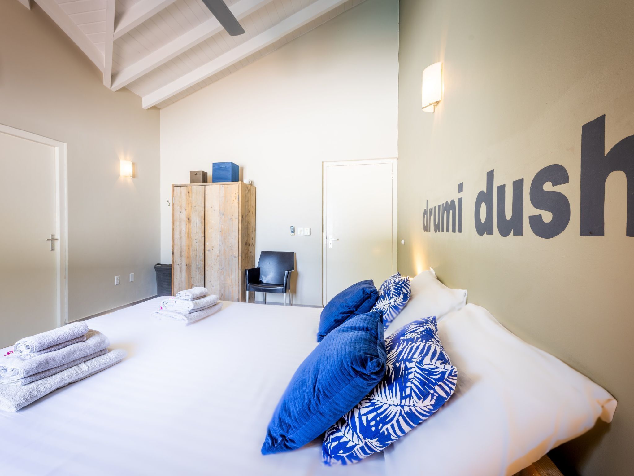 Habitación de hotel con cama, armario, silla y una pared con el texto "drumi dus".