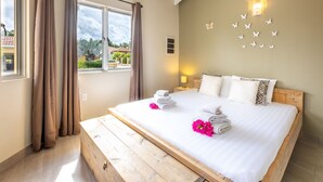 A bedroom with a large bed, curtains, a wooden bench, a wall-mounted light, and a view of the outside. - Villa Drumi Dushi met privé zwembad by Interhome (Jan Thiel)