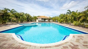 A large, clear swimming pool with a tiled edge, surrounded by palm trees and a covered pavilion. - Villa Drumi Dushi met privé zwembad by Interhome (Jan Thiel)