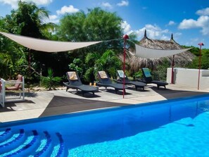 Un área de piscina con sillas de descanso y una estructura de techo de paja.