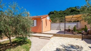 A small orange building with a satellite dish, a stone patio, and a covered outdoor seating area with potted plants.