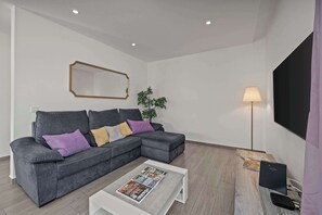 A living room with a grey sectional sofa, a white coffee table, a floor lamp, and a flat-screen TV. - Elegant Flat with Balcony in Lagos by HostWise (Lagos)
