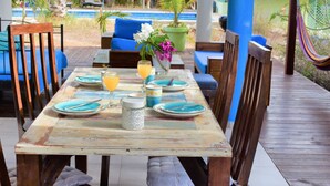Une terrasse en bois avec une table dressée pour deux personnes, entourée de chaises et d’un hamac.