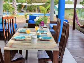 Una terraza de madera con una mesa para dos, sillas y una hamaca.