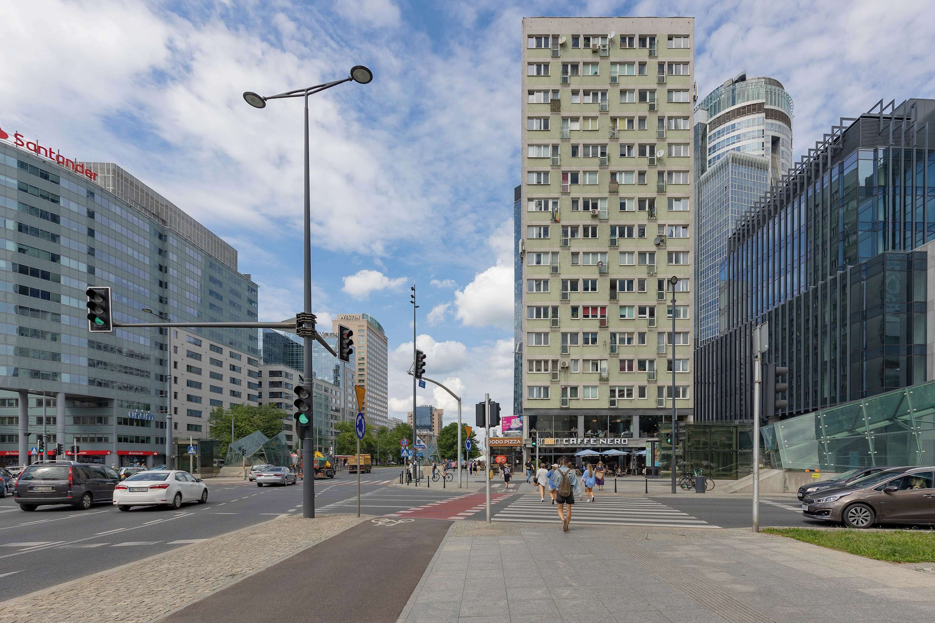 A city street with modern buildings, a pedestrian crossing, and traffic lights.