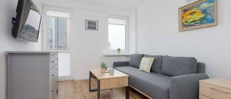 A modern living room with a grey sofa, a wooden coffee table, a grey cabinet, and a flat-screen TV mounted on the wall.