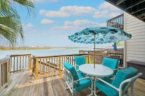 A wooden deck with a table and chairs, overlooking a body of water. - Waterfront Island Escape | Balcony, Boat Slips & Pool (Corpus Christi)
