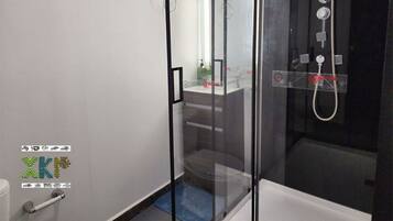 Un baño moderno con ducha de vidrio, lavamanos a la vista y un inodoro.