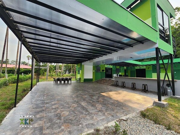 An outdoor covered patio area with a stone floor, a seating arrangement, and a bar counter.
