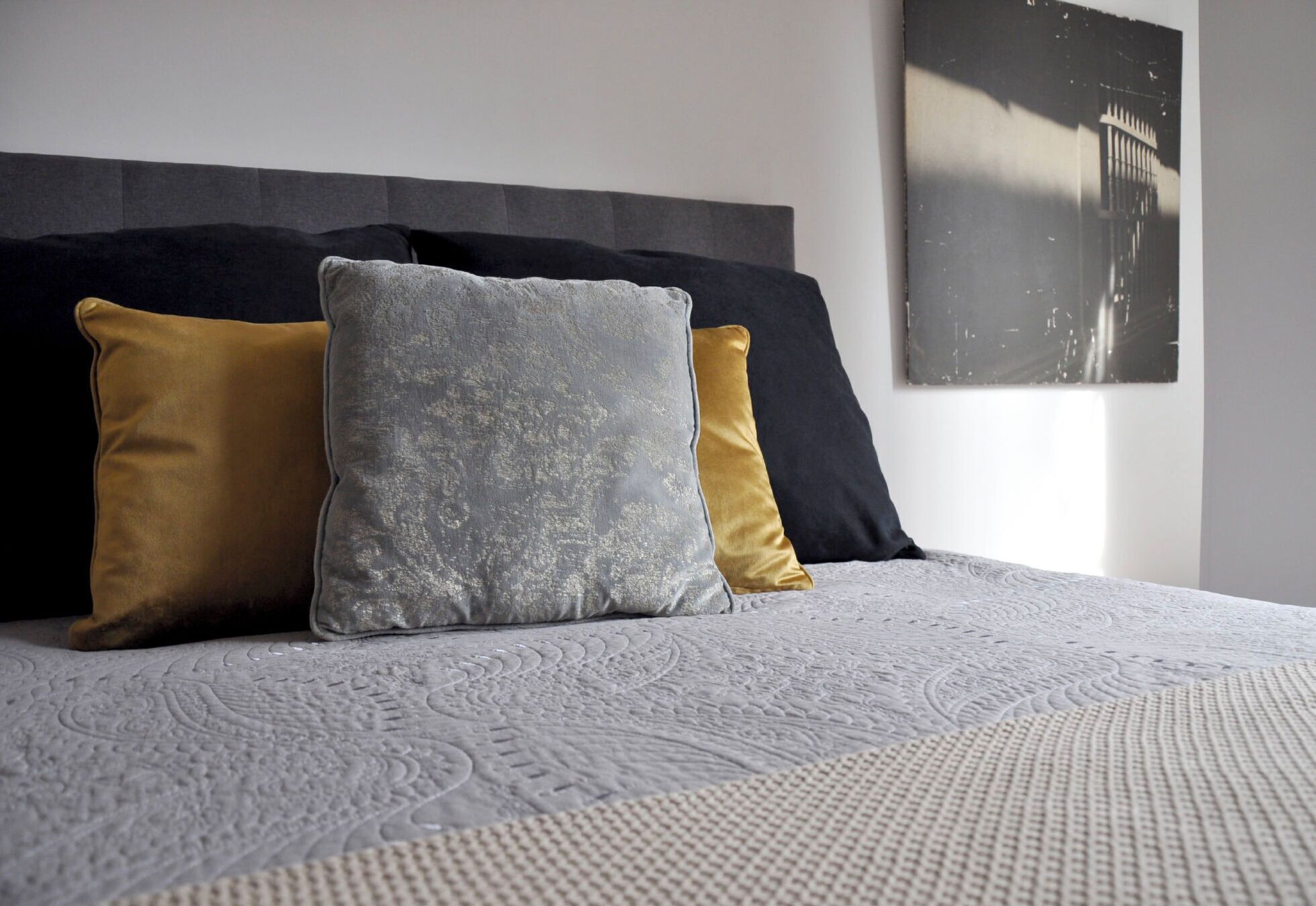 A bed with a textured white bedspread and three pillows in different colors.