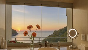 Een badkamer met een groot raam, een wastafel, een spiegel en een vaas met bloemen.