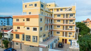 Un hotel de varios pisos con balcones, zona de estacionamiento y entrada con portón.